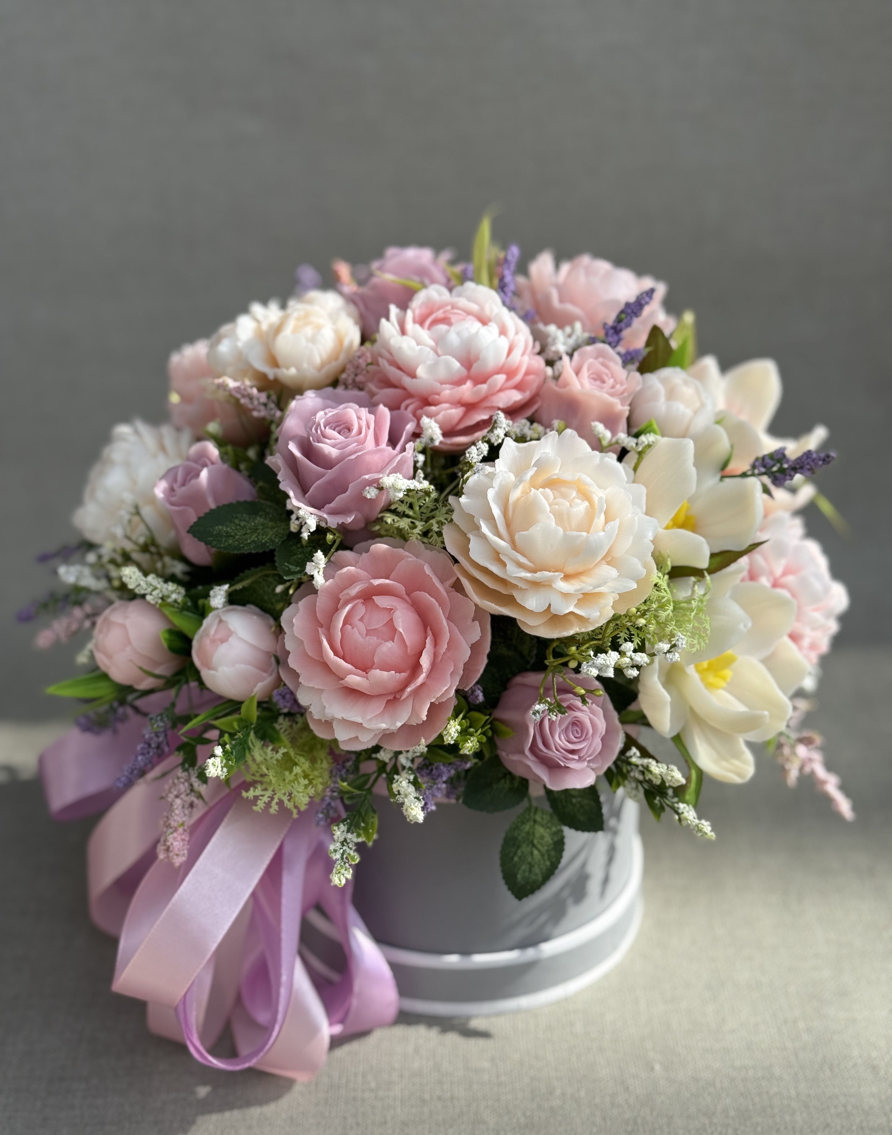 Large pastel soap flower bouquet with pink peonies, lilac roses and cream magnolias in a grey hat box with a lilac bow.